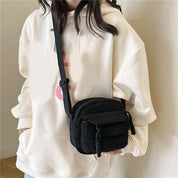 Donna con felpa bianca indossa borsa a tracolla nera in velluto a coste. Accessorio moda casual, ideale per look quotidiani e shopping.