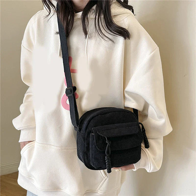 Donna con felpa bianca indossa borsa a tracolla nera in velluto a coste. Accessorio moda casual, ideale per look quotidiani e shopping.