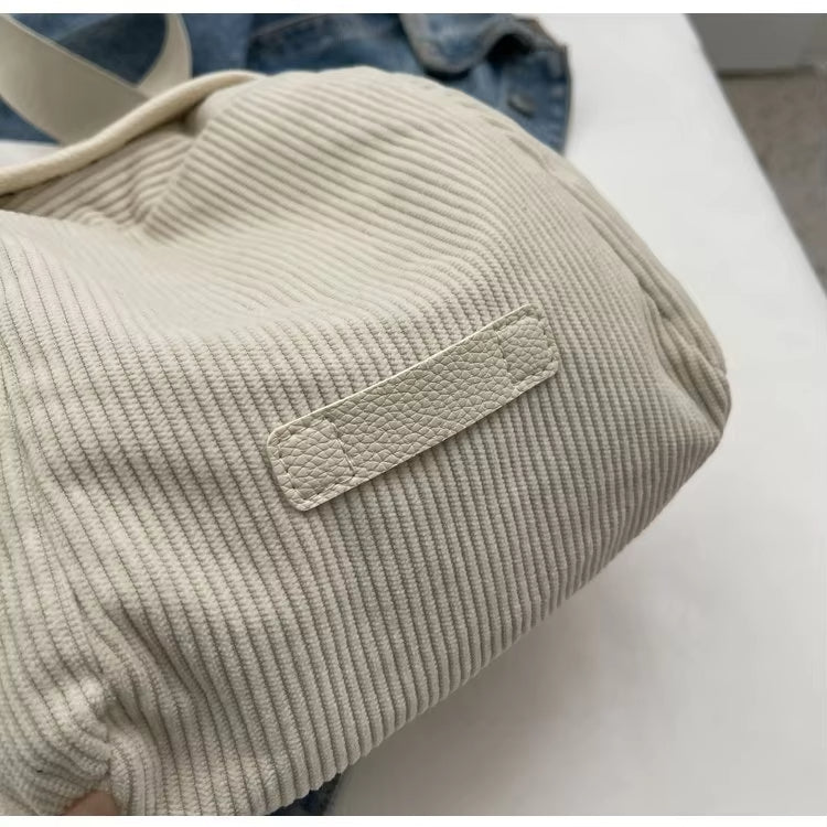 Borsa a tracolla in tessuto a coste beige, dettaglio etichetta in pelle. Accessorio moda casual, ideale per shopping e uso quotidiano.