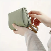 Mani che tengono un elegante astuccio verde in tessuto, chiuso con zip e cinturino in pelle. Accessorio moda, portafoglio compatto, design minimalista.