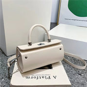 Borsa a mano in pelle bianca con tracolla regolabile, design elegante e moderno, posizionata su un libro, ideale per moda femminile e shopping.