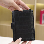 Portafoglio nero in pelle con motivo coccodrillo, tenuto in mano. Design elegante e moderno, ideale per uomo e donna. Accessorio di moda.