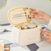 Astuccio cosmetico beige aperto con pennelli trucco e contenitori, su tavolo moderno. Accessori bellezza, organizzazione trucco, eleganza.