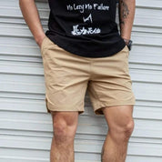 Uomo in pantaloncini beige e maglietta nera con scritte bianche, posa casual davanti a una porta metallica. Moda estiva, abbigliamento casual uomo.