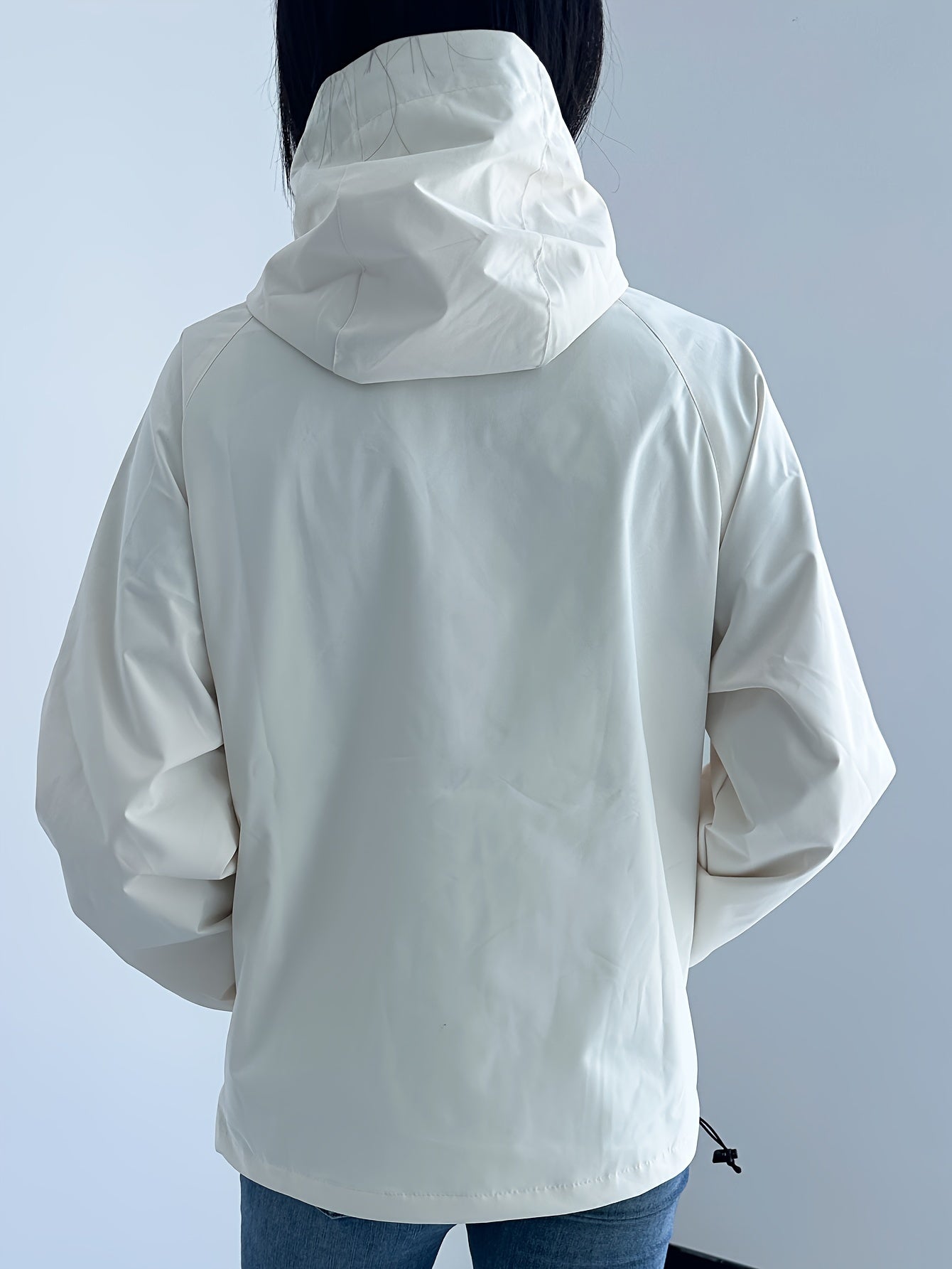 Giacca impermeabile bianca da donna con cappuccio, vista posteriore. Design moderno, ideale per attività all'aperto. Tessuto resistente all'acqua.