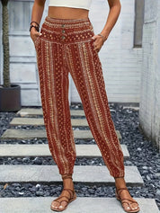Pantaloni boho a vita alta con stampa etnica rossa, tasche laterali, indossati con sandali marroni. Stile casual estivo per donna.