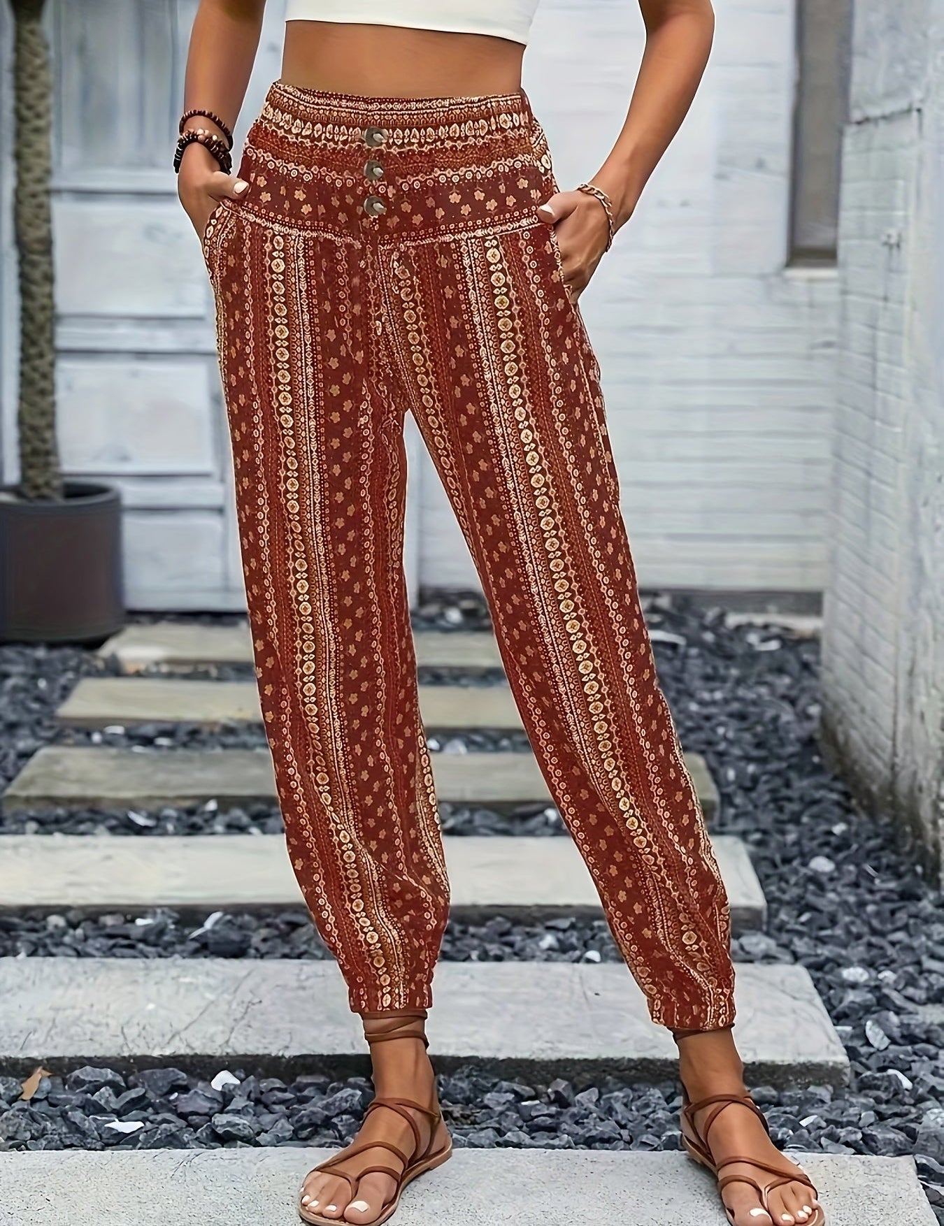 Pantaloni boho a vita alta con stampa etnica rossa, tasche laterali, indossati da una donna con sandali marroni. Moda estiva casual.