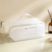 Borsa cosmetica bianca trasparente con cerniera, manico superiore, su tavolo da toeletta. Ideale per organizzare trucchi e accessori da viaggio.