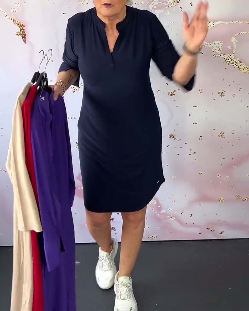 Donna in abito blu scuro, maniche a tre quarti, tiene abiti colorati su grucce. Sfondo rosa chiaro. Moda femminile, abbigliamento casual elegante.