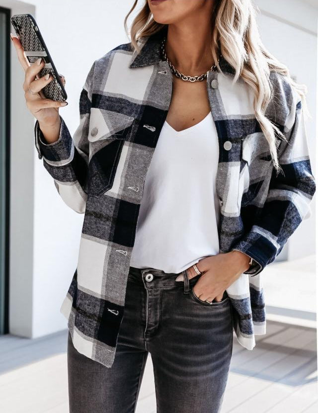 Donna con camicia a quadri bianca e nera, t-shirt bianca e jeans grigi, tiene uno smartphone. Moda casual autunnale, outfit trendy.