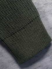 Manica maglione verde scuro in maglia a coste su sfondo grigio. Tessuto caldo e morbido, ideale per l'inverno. Moda uomo, abbigliamento casual.