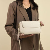 Donna con borsa a tracolla beige in pelle, design elegante e minimalista, indossata con giacca marrone. Accessorio moda femminile di tendenza.