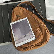 Zaino a tracolla marrone con tasca frontale su panca grigia, tablet bianco appoggiato sopra. Accessori moda, tecnologia portatile, design moderno.