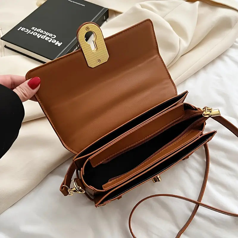 Borsa a tracolla in pelle marrone aperta, con scomparti interni e chiusura dorata. Accessorio moda elegante per donna.