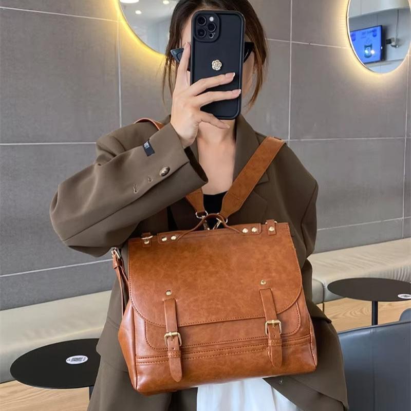 Borsa a tracolla in pelle marrone, design elegante con fibbie, indossata da una persona in giacca marrone. Accessorio moda donna, stile casual.