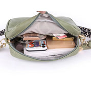 Borsa a tracolla verde aperta, mostra contenuto: smartphone, trucchi, portafoglio, chiavi. Design moderno, tracolla leopardata. Accessorio moda donna.