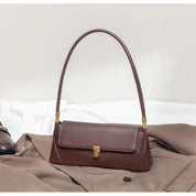 Borsa a spalla marrone in pelle su cappotto beige, design elegante e moderno, accessorio moda donna, chiusura con fibbia dorata.