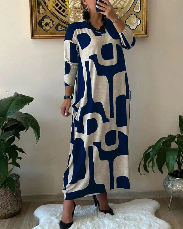 Abito lungo donna a maniche lunghe con stampa geometrica blu e beige, stile casual chic, perfetto per moda autunnale. Arredamento moderno sullo sfondo.