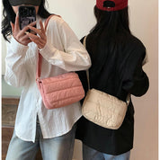 Due donne con borse a tracolla imbottite, una rosa e una beige, indossano camicie casual. Moda femminile, accessori trendy, stile urbano.
