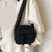 Borsa a tracolla nera in velluto a coste, indossata su felpa bianca. Design compatto, ideale per moda casual e streetwear. Accessorio unisex.