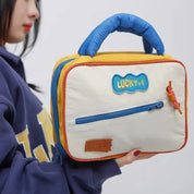 Borsa termica portapranzo in tessuto beige con manico blu, dettagli gialli e rossi, tasca frontale con zip, logo "LUCKY+1". Ideale per scuola o ufficio.
