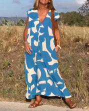 Donna con abito lungo estivo blu e bianco, motivo astratto, in piedi su strada di campagna. Sandali marroni, sfondo naturale. Moda casual estiva.