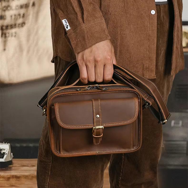 Borsa a tracolla in pelle marrone, design vintage, con fibbia e tasca frontale. Accessorio moda uomo, ideale per lavoro e tempo libero.