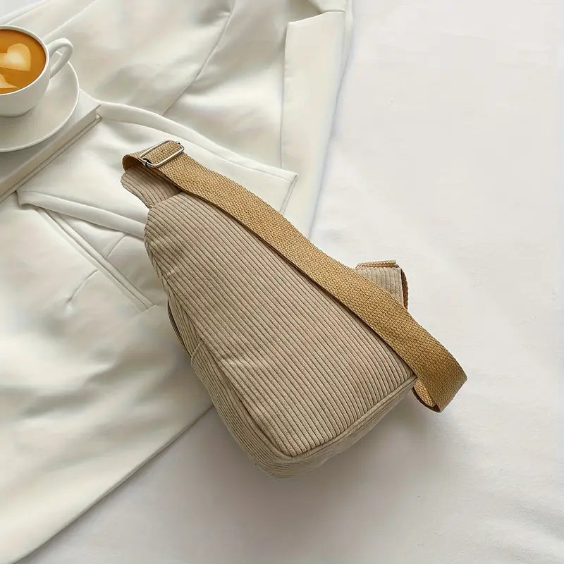 Marsupio beige a coste su tessuto bianco, con tazza di caffè. Design elegante, tracolla regolabile. Accessorio moda casual e versatile.