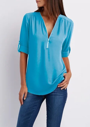 Blusa donna azzurra con zip, maniche a 3/4 arrotolabili, scollo a V, abbinata a jeans. Moda casual elegante, abbigliamento femminile trendy.