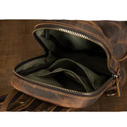 Zaino in pelle marrone vintage aperto, con scomparti interni visibili. Design robusto, ideale per viaggi e uso quotidiano. Accessorio moda uomo.
