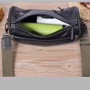 Borsa a tracolla in pelle nera con cerniera aperta, contenente un libro verde. Design elegante, ideale per uomo e donna. Accessorio moda versatile.