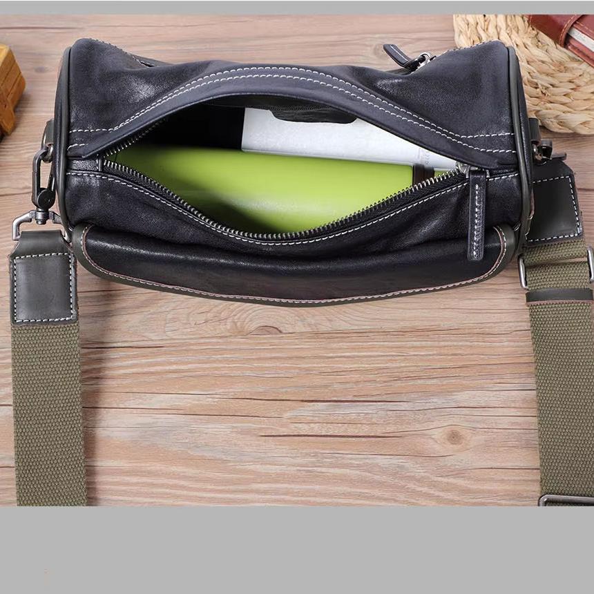Borsa a tracolla in pelle nera con cerniera aperta, contenente un libro verde. Design elegante, ideale per uomo e donna. Accessorio moda versatile.