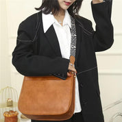 Donna con borsa a tracolla in pelle marrone, indossa giacca nera e camicia bianca. Moda femminile, accessori eleganti, stile casual chic.