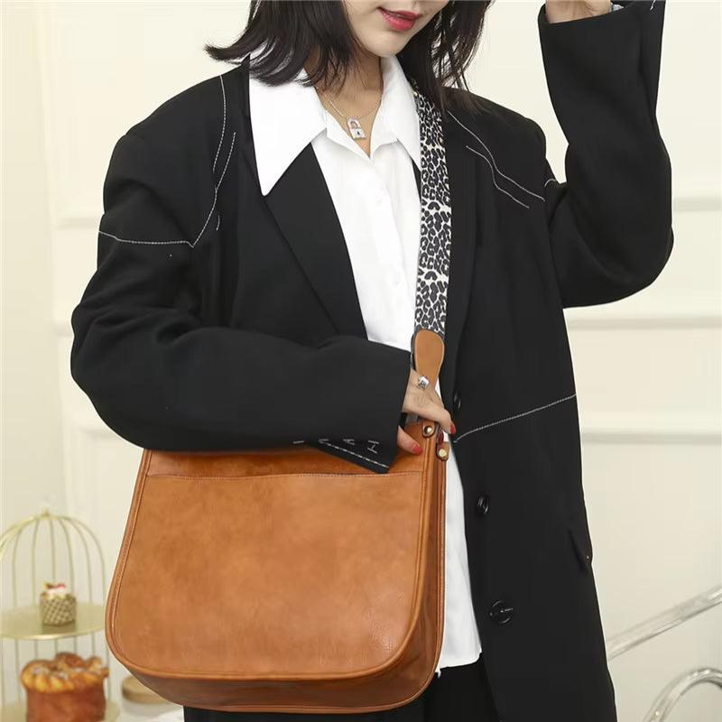 Donna con borsa a tracolla in pelle marrone, indossa giacca nera e camicia bianca. Moda femminile, accessori eleganti, stile casual chic.