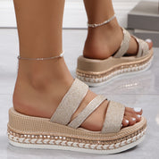 Sandali platform donna con cinturini glitterati, suola intrecciata, colore beige, indossati su pavimento bianco. Scarpe estive moda 2023.