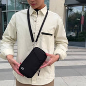 Uomo con camicia beige indossa una borsa a tracolla nera, ideale per smartphone e accessori. Moda urbana, accessorio pratico e versatile.