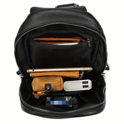 Zaino in pelle nera aperto, mostra tasche interne con smartphone, portafoglio, power bank e chiavi. Accessori organizzati per viaggio e lavoro.