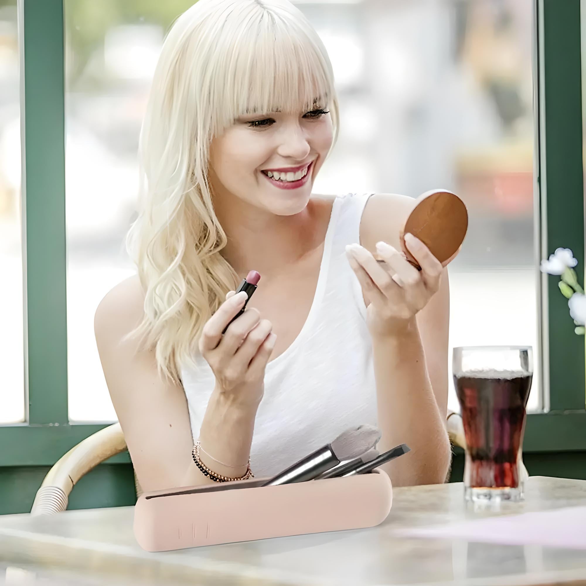 Bionda sorridente applica rossetto rosa davanti a specchietto, seduta in caffetteria. Trucco, bellezza, cosmetici, lifestyle.