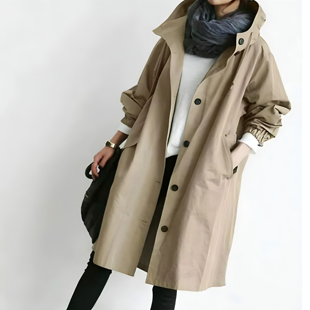 Cappotto trench beige donna, lungo, con bottoni neri, abbinato a sciarpa grigia e pantaloni neri. Moda autunnale elegante e casual.