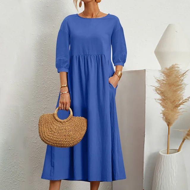 Abito lungo blu donna con maniche a tre quarti, borsa paglia intrecciata, sfondo bianco minimalista, moda estiva elegante e casual.