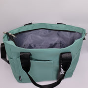 Borsa tote verde acqua con manici neri, tasca frontale e chiusura a zip. Design moderno, ideale per shopping e uso quotidiano.