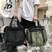 Due borse a tracolla unisex, una nera e una verde, con manici robusti e tasche multiple, indossate da due persone in abbigliamento casual.