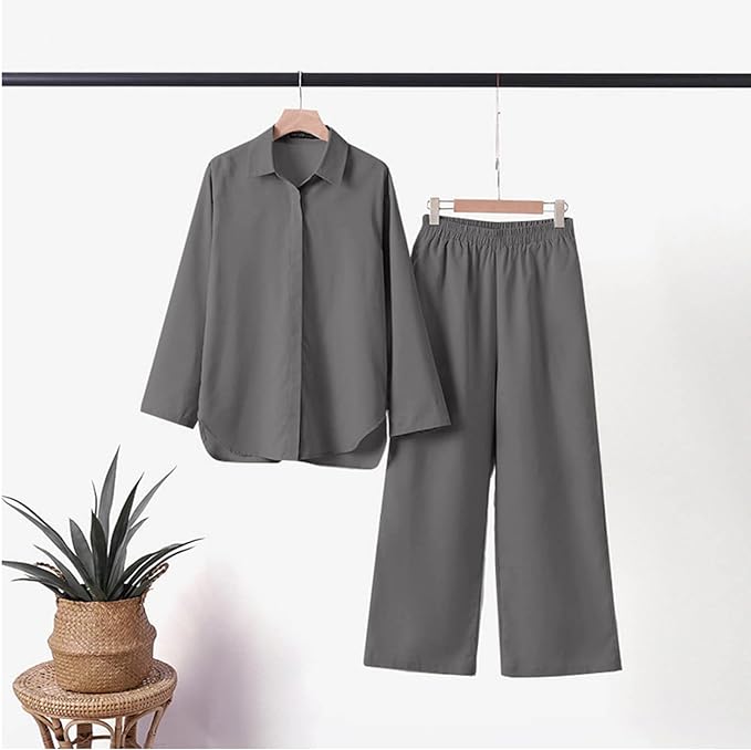 Camicia e pantaloni grigi da donna su appendiabiti, stile casual, tessuto leggero, pianta decorativa, sfondo bianco, moda minimalista.