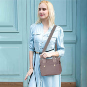 Donna con borsa a tracolla in pelle marrone chiaro, abito azzurro, sfondo porta blu. Accessorio moda elegante, stile casual chic.