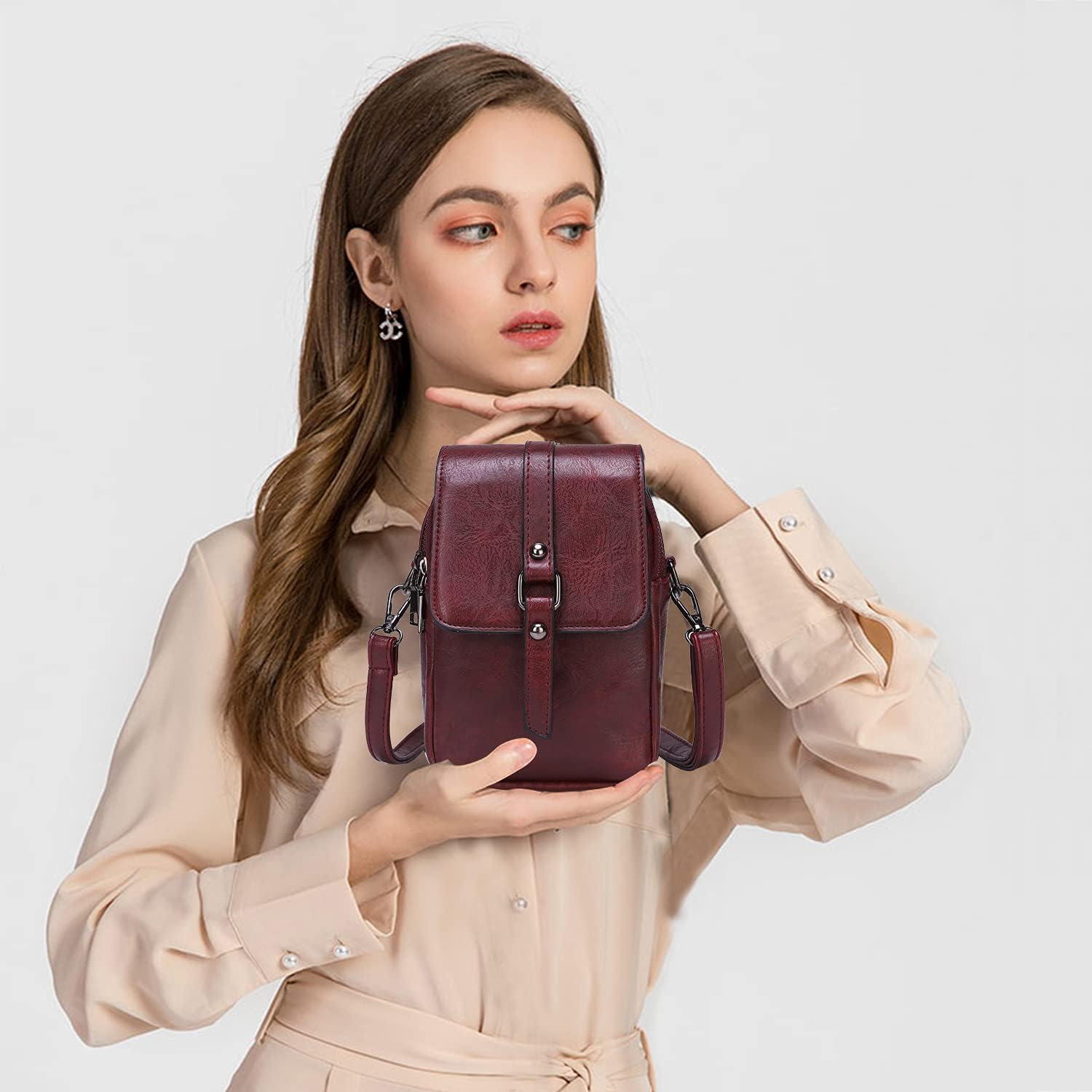 Donna con borsa a tracolla in pelle bordeaux, design elegante e moderno, abbigliamento beige, sfondo bianco. Accessorio moda femminile.