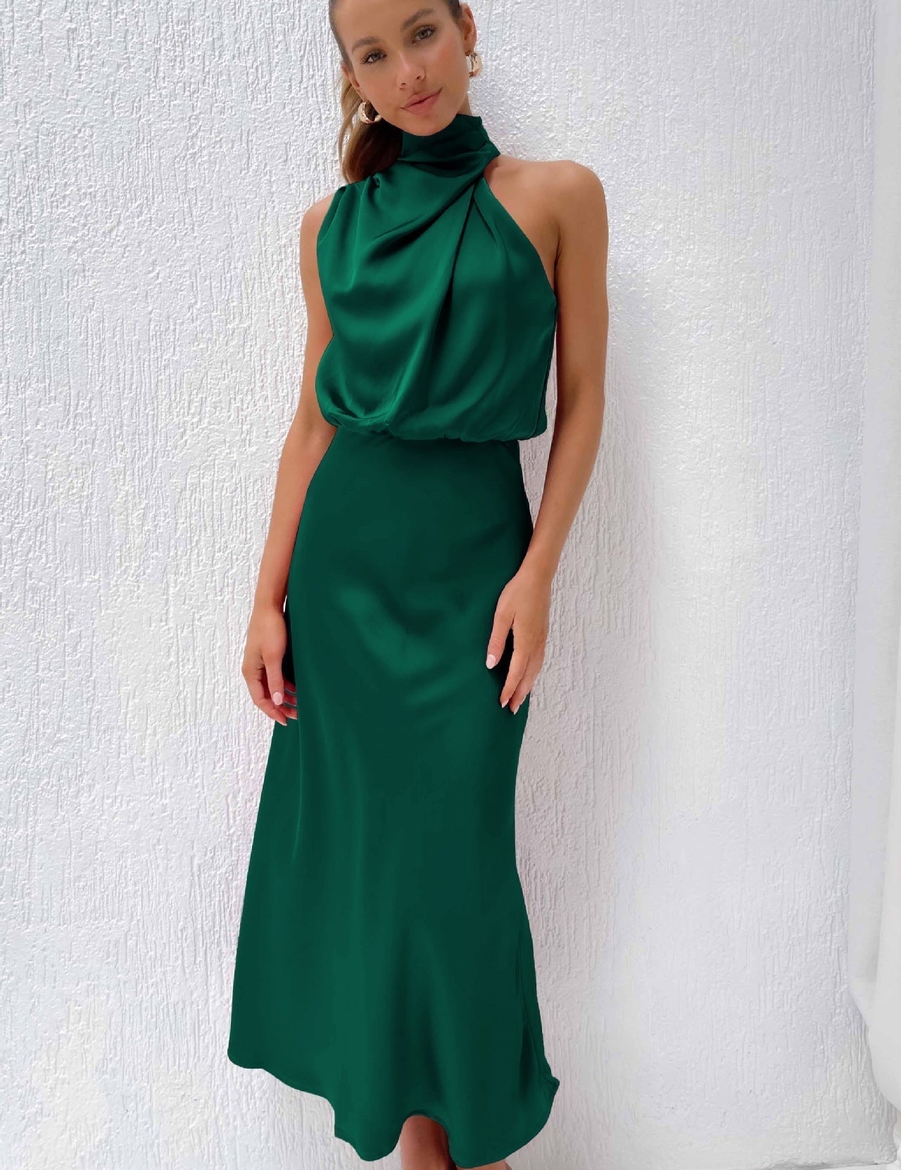 Abito lungo verde smeraldo elegante, senza maniche, con collo alto drappeggiato, indossato da una donna. Perfetto per eventi formali e serate.