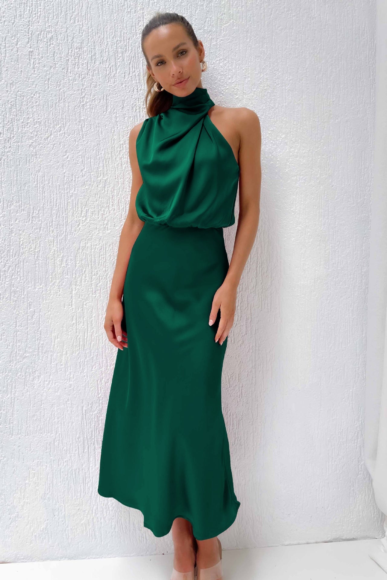 Abito lungo verde smeraldo elegante, senza maniche, con collo alto drappeggiato, indossato da una donna. Perfetto per eventi formali e serate.