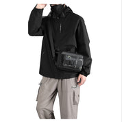 Giacca nera impermeabile uomo, mascherina nera, pantaloni cargo beige, borsa a tracolla nera. Abbigliamento outdoor, moda urbana.