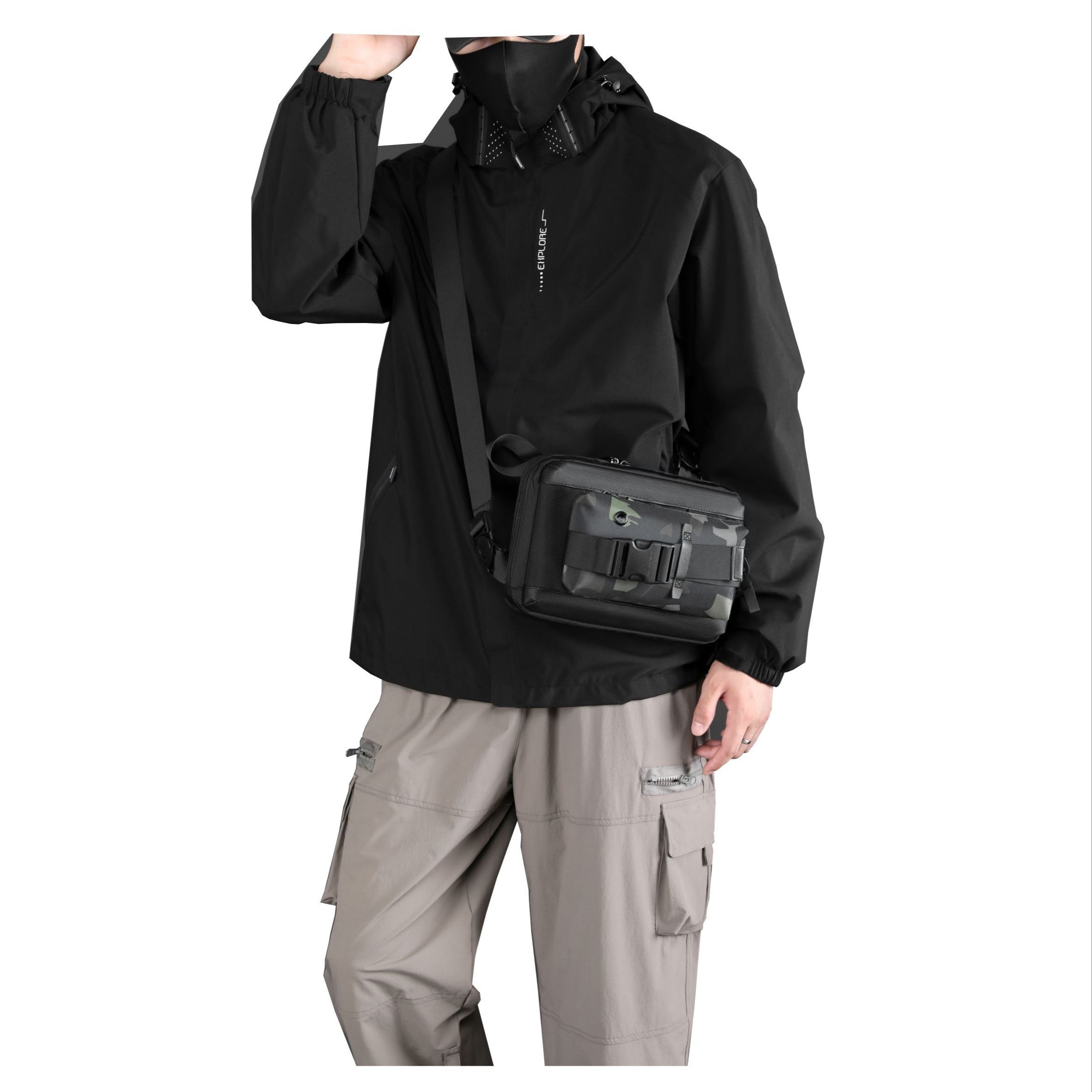 Giacca nera impermeabile uomo, mascherina nera, pantaloni cargo beige, borsa a tracolla nera. Abbigliamento outdoor, moda urbana.