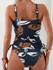 Costume intero donna con stampa foglie tropicali, spalline regolabili, colore blu scuro e marrone, moda mare estate 2023.